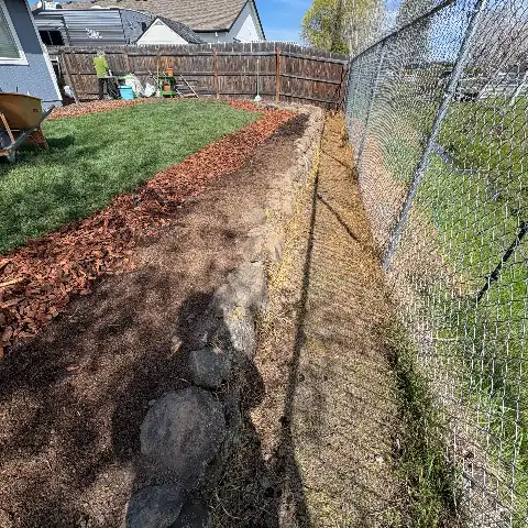 same backyard after service with a fresh bark-mulch bed along the cleaned rock wall